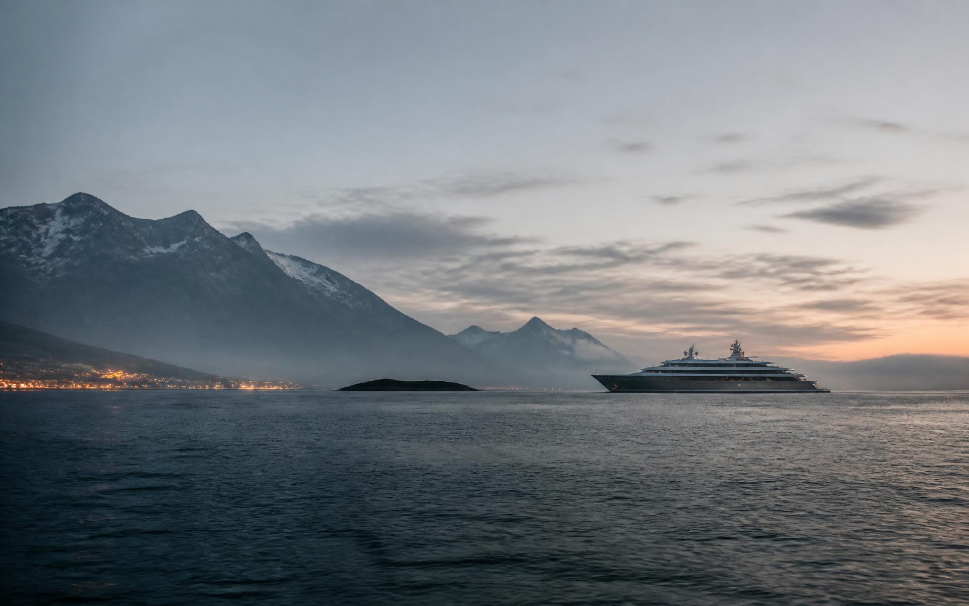 Dawn over a quiet ocean with a distant expedition vessel and misted mountains